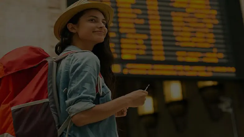 Traveller in a straw hat with a backpack at an airport departure board