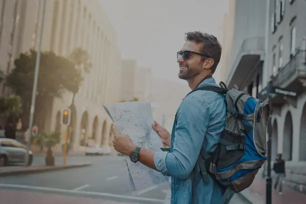 Smiling traveller with a backpack reading a map in a city street